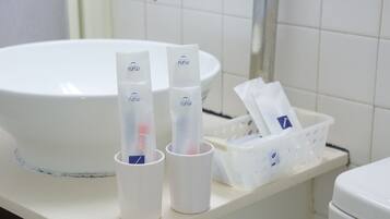 Uma pia de banheiro com duas xícaras brancas e uma cesta plástica com artigos de higiene pessoal.