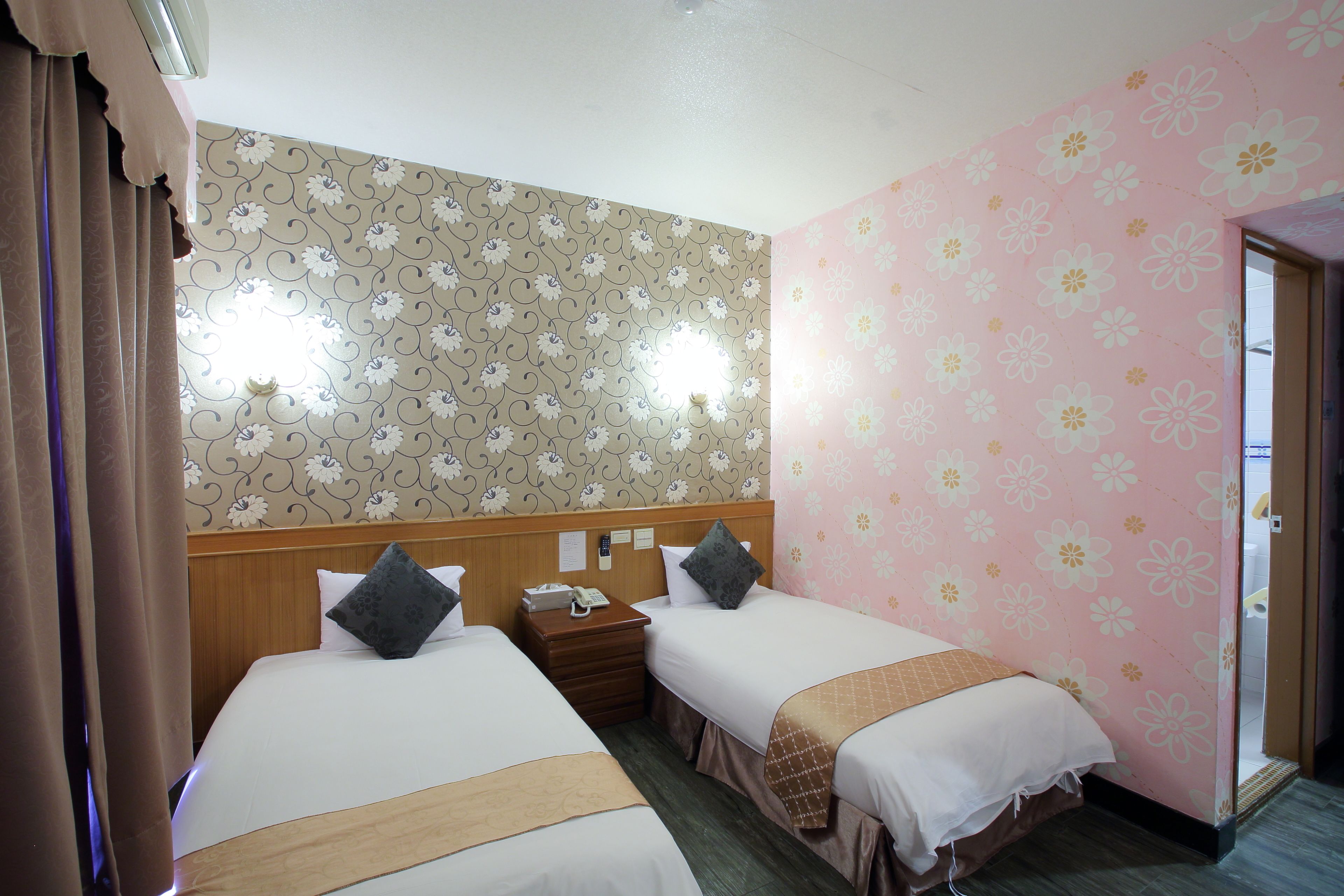 Habitación de hotel con dos camas, cabecera de madera, mesita de noche y baño visible a través de una puerta abierta.