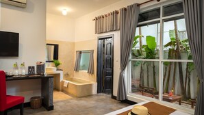 A modern bathroom with a bathtub, shower, and toilet. There is a sink with a mirror, a red chair, and a window with curtains. - Landing Zone Boutique Hotel (Siem Reap)