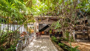A covered outdoor area with a brick pathway, bicycles, and potted plants. - Landing Zone Boutique Hotel (Siem Reap)