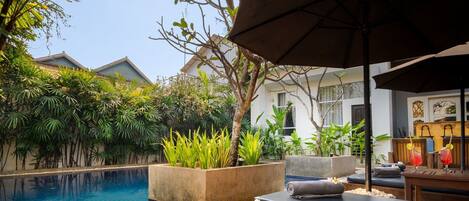 A poolside area with lounge chairs, a table with drinks, and a large umbrella.
