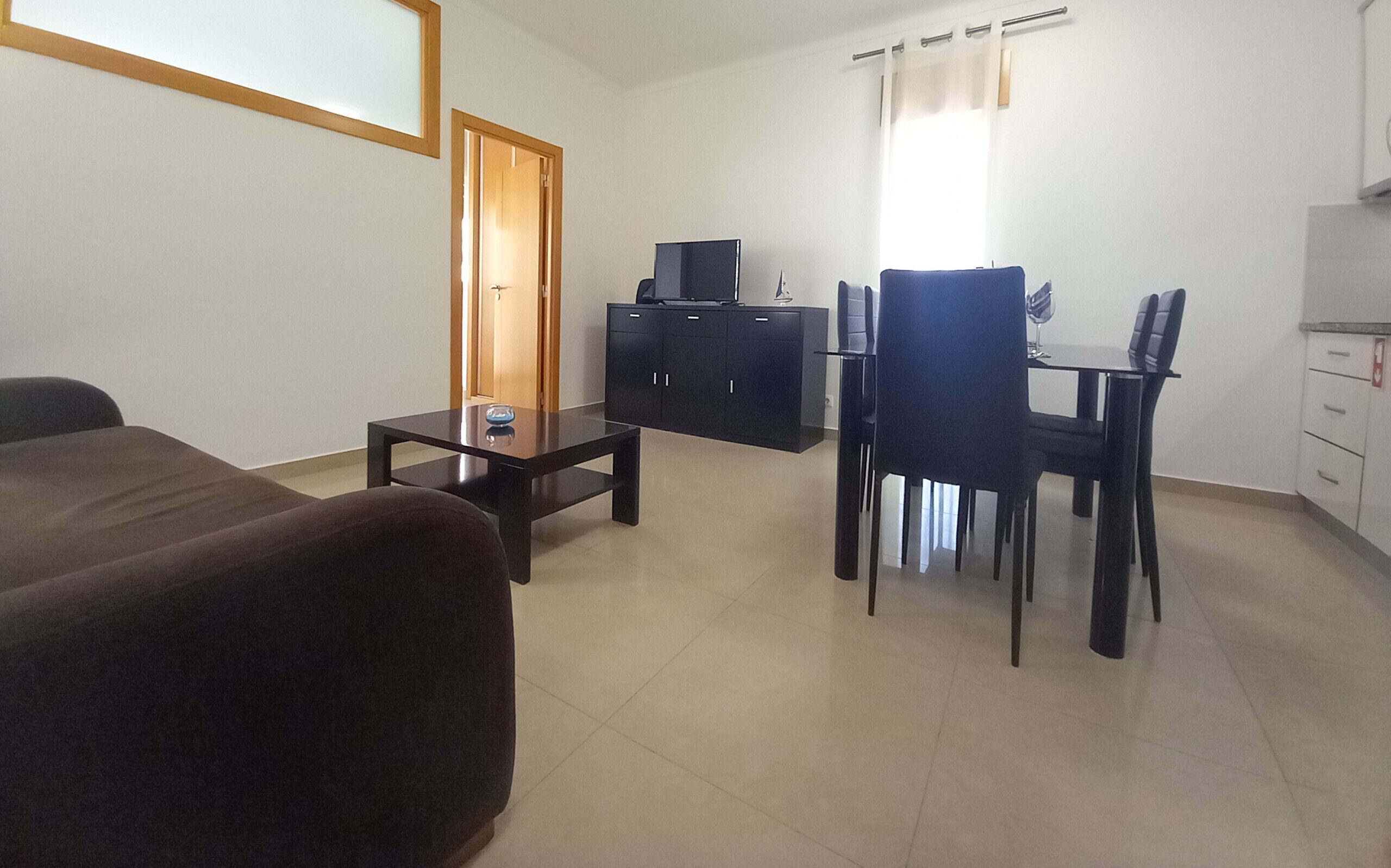 Una habitación con cama, una mesita, un armario, una silla y una mesa de comedor con sillas.