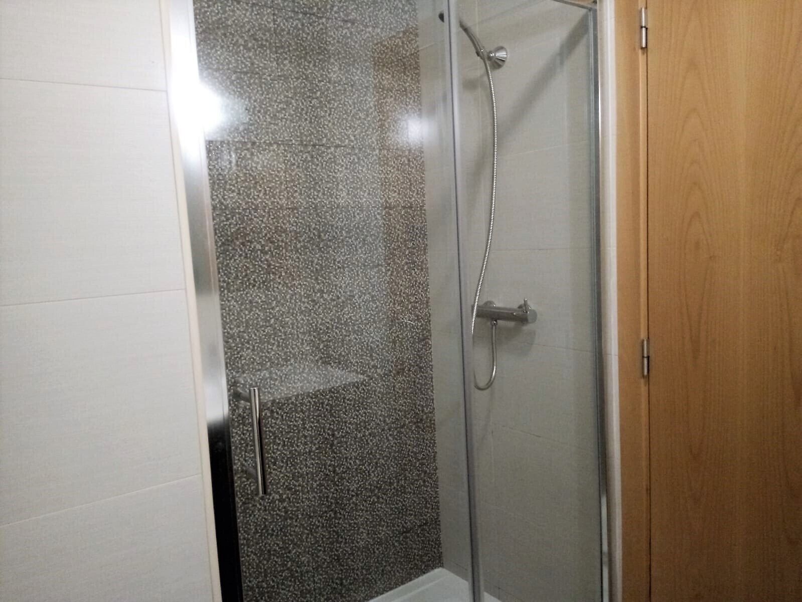 A glass-enclosed shower with a showerhead and a handheld shower attachment.