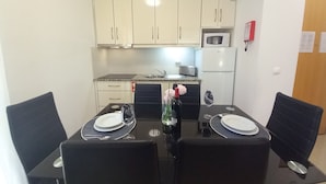 Un comedor con una mesa dispuesta para cuatro personas, con platos, vasos y una botella. La habitación cuenta con armarios color crema, un microondas y un refrigerador.