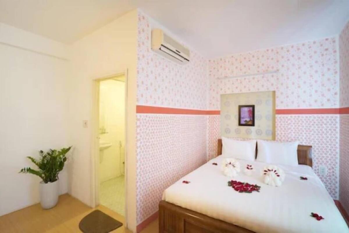 A hotel room with a bed, a potted plant, an air conditioning unit, and a framed picture on the wall.