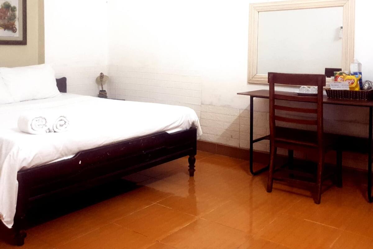 A room with a bed, a desk, a chair, a mirror, and a picture on the wall.
