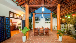 A covered outdoor seating area with brick flooring, wooden pillars, and hanging lights. - Cua Dai Beach Homestay (Da Nang)