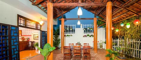 A covered outdoor seating area with brick flooring, wooden pillars, and hanging lights.