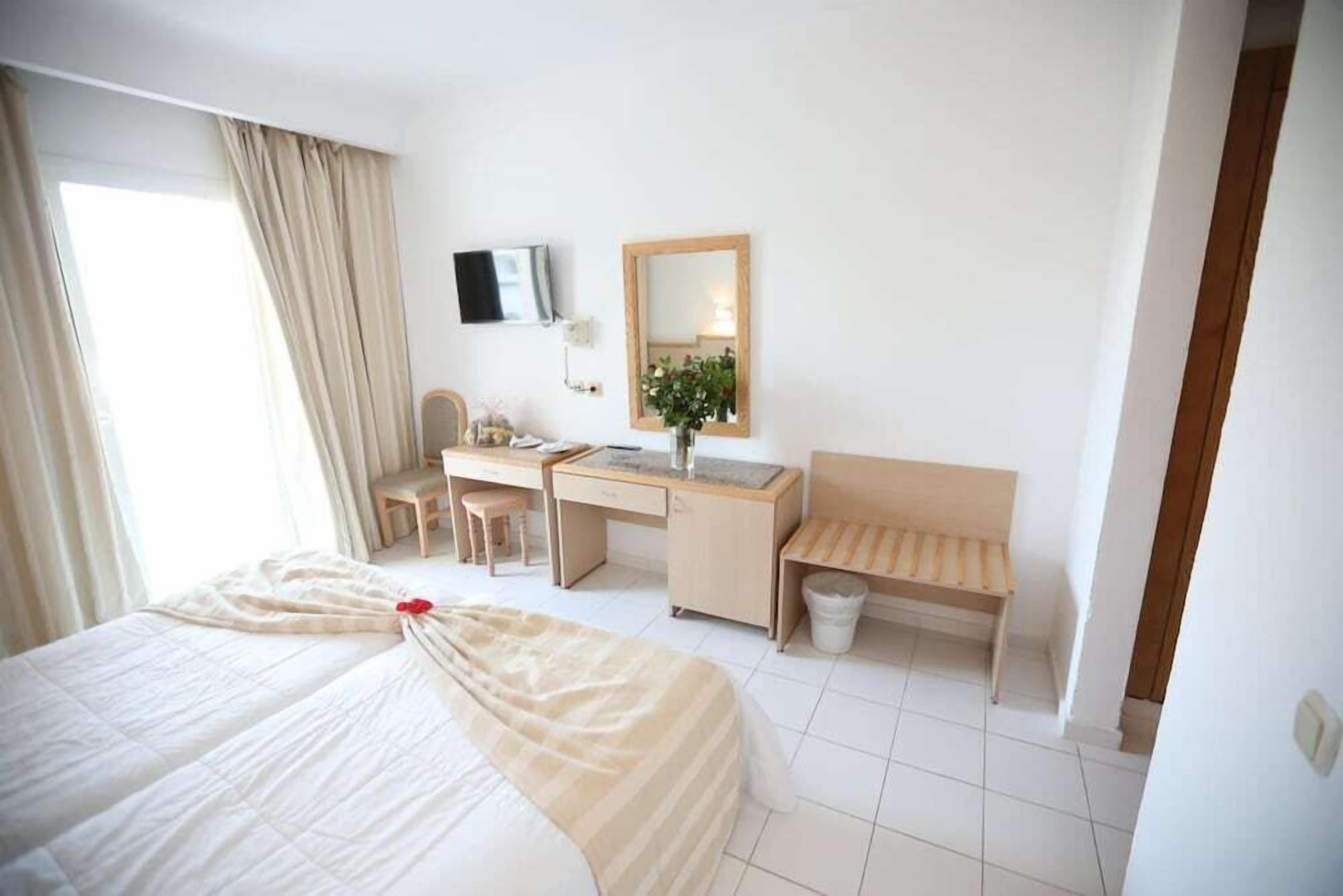 A hotel room with a bed, desk, chair, and a small bench.