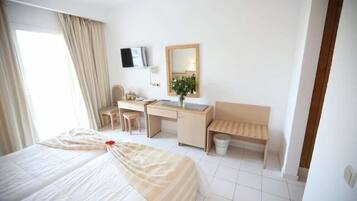 A hotel room with a bed, desk, chair, and a small bench.