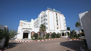 A large, white building with the sign "Royal Jumeirah" on top. It has multiple balconies and a central entrance with a covered area. - Hotel Royal Jinene (Sousse)