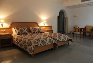 A bedroom with a bed, two bedside lamps, a chair, and a door. - Hotel Royal Jinene (Sousse)