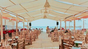 A beachside restaurant with wooden tables and chairs, a covered seating area, and a view of the ocean. - Hotel Royal Jinene (Sousse)