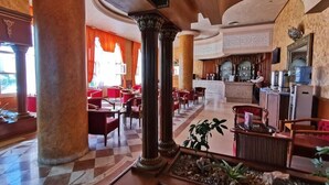 A hotel lobby with a checkered floor, red chairs, a reception desk, and a bar area. - Hotel Royal Jinene (Sousse)