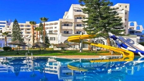 A swimming pool with a water slide, surrounded by a building with balconies and palm trees. - Hotel Royal Jinene (Sousse)