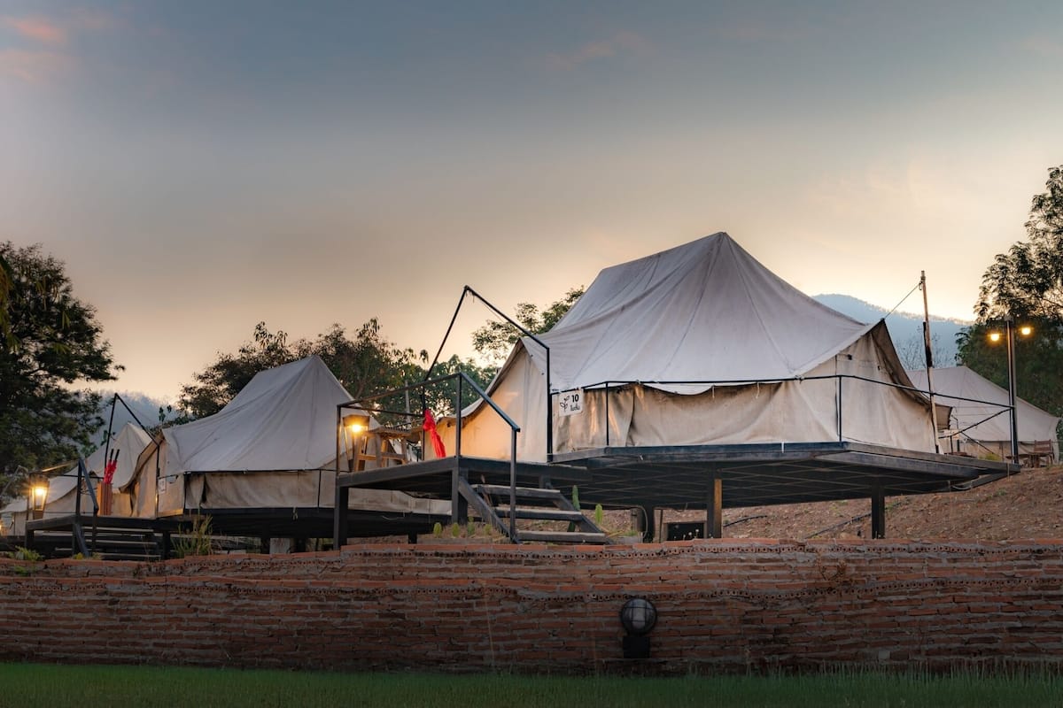 A series of tents with a flat roof, wooden platforms, and a brick wall in the foreground.
