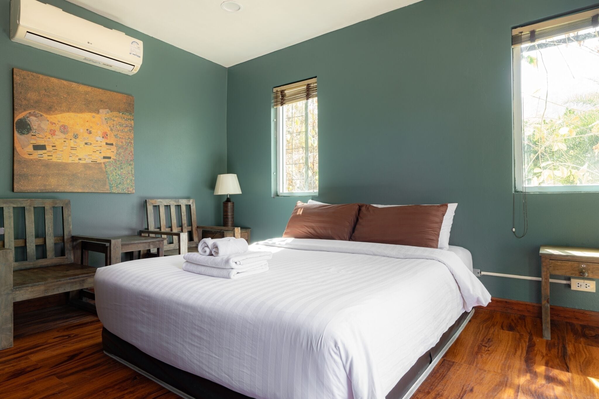 A bedroom with a large bed, a wooden bench, a table, and a painting on the wall.