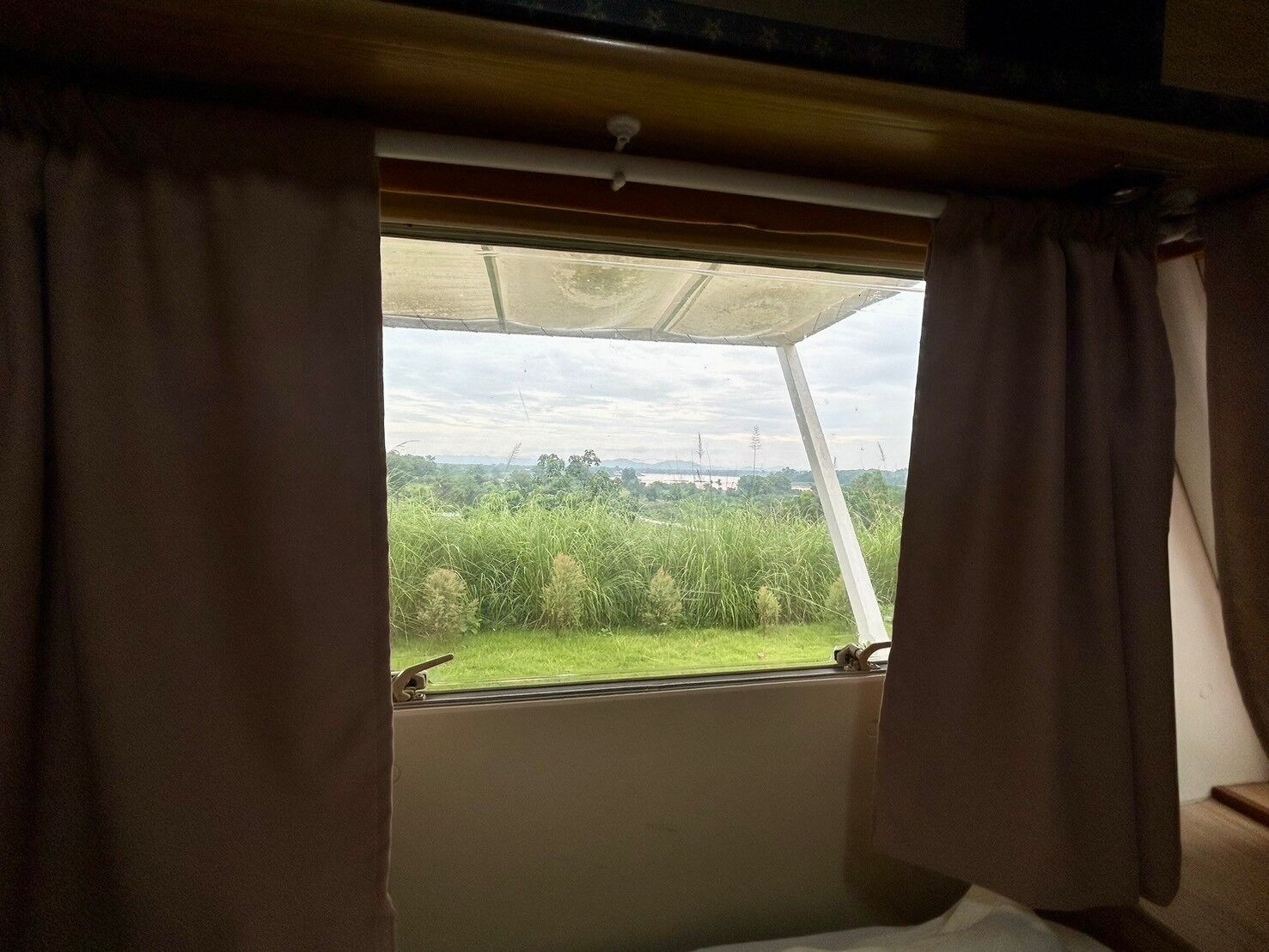A window with curtains, a view of greenery and distant buildings.