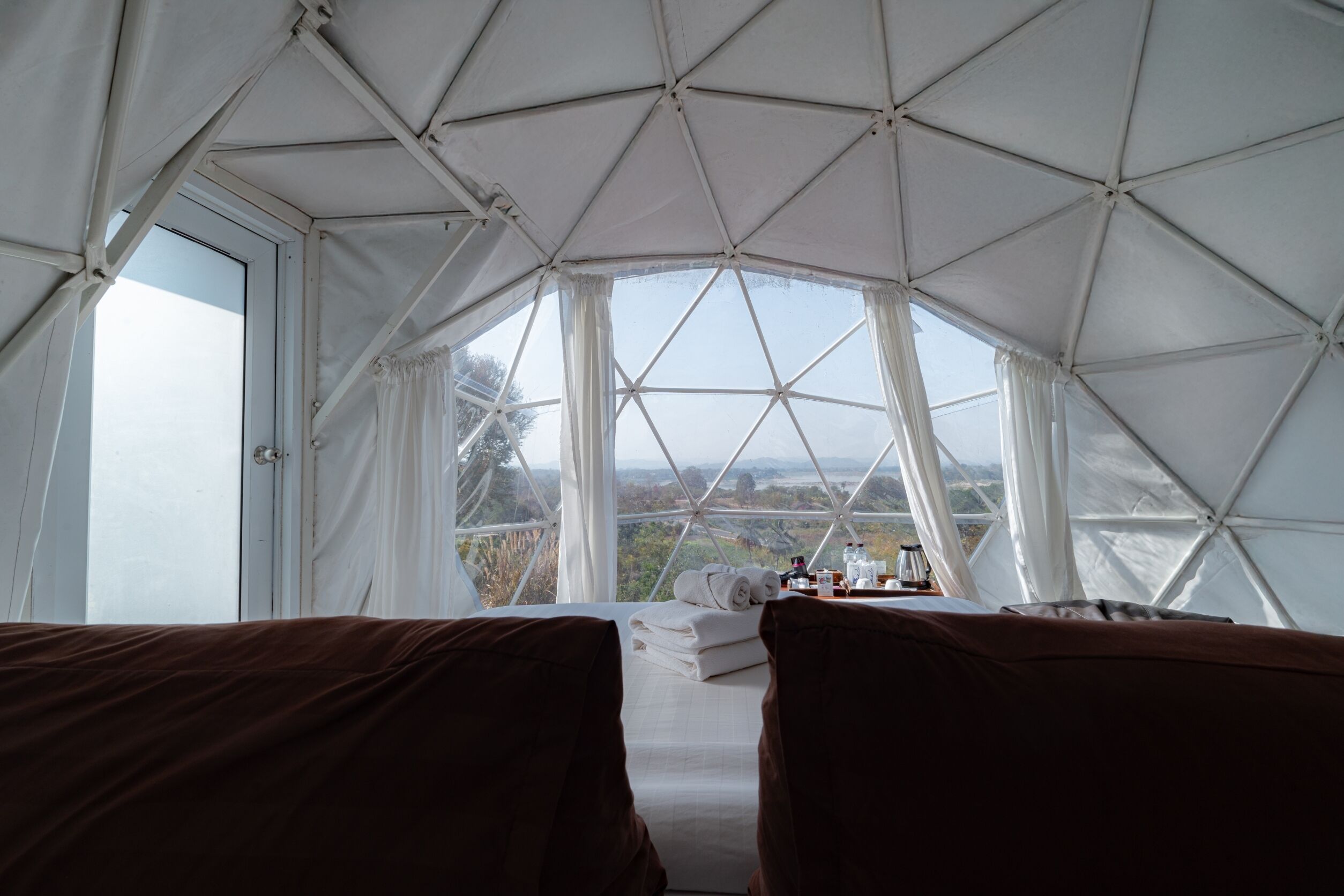 Habitación con estructura de techo geométrica, ventanas amplias, cama con ropa blanca y vistas al exterior.
