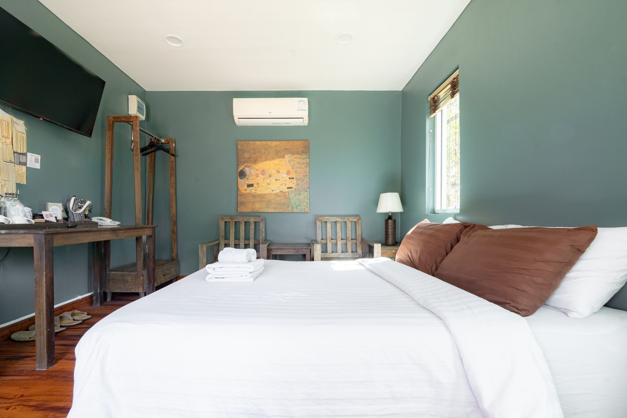 A bedroom with a bed, a desk with a telephone, a lamp, and a painting on the wall.