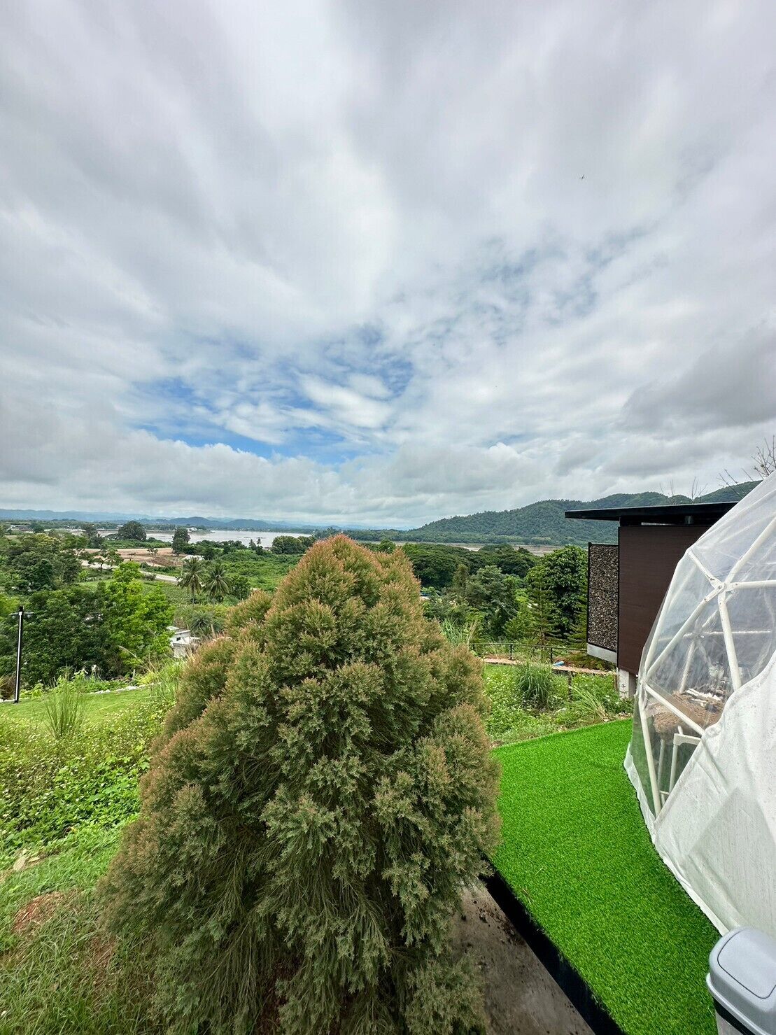 A garden with a greenhouse, a lawn, and a view of distant hills.