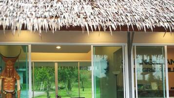 A modern building with a thatched roof, large glass windows, and two white chairs outside.
