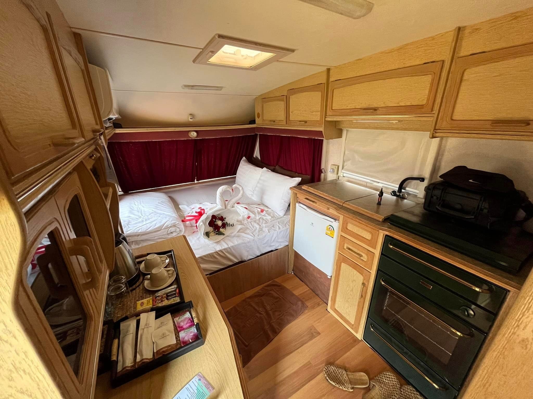Interior compacto de una caravana con cama, kitchenette y un refrigerador pequeño.