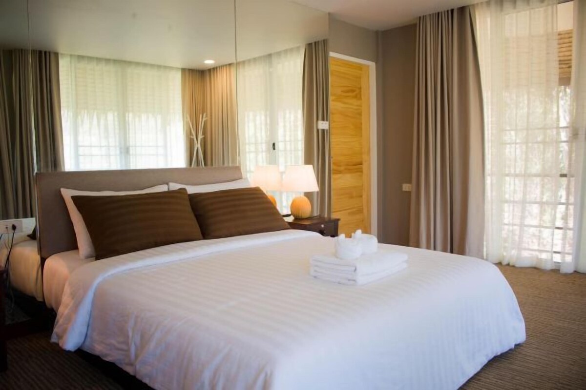 Una habitación de hotel con una cama grande, una mesita de noche con lámpara y cortinas en las ventanas.