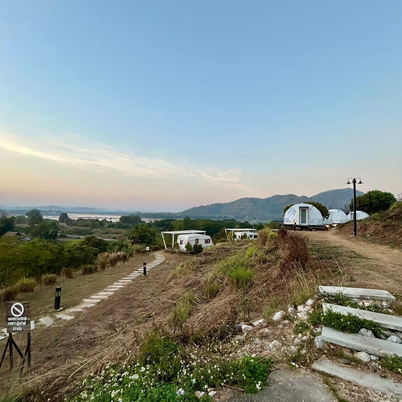 A campsite with dome-shaped tents, a dirt path leading to them, and a view of distant hills.