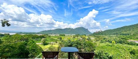 A terrace with two chairs and a table, overlooking a lush landscape with hills and a clear sky.