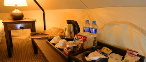 Habitación con tienda de campaña, una mesa con aperitivos, una tetera y agua embotellada.