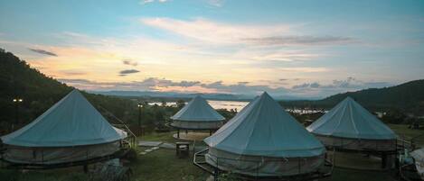 Three dome-shaped tents set up in a grassy area with a scenic view of hills and a body of water in the background.