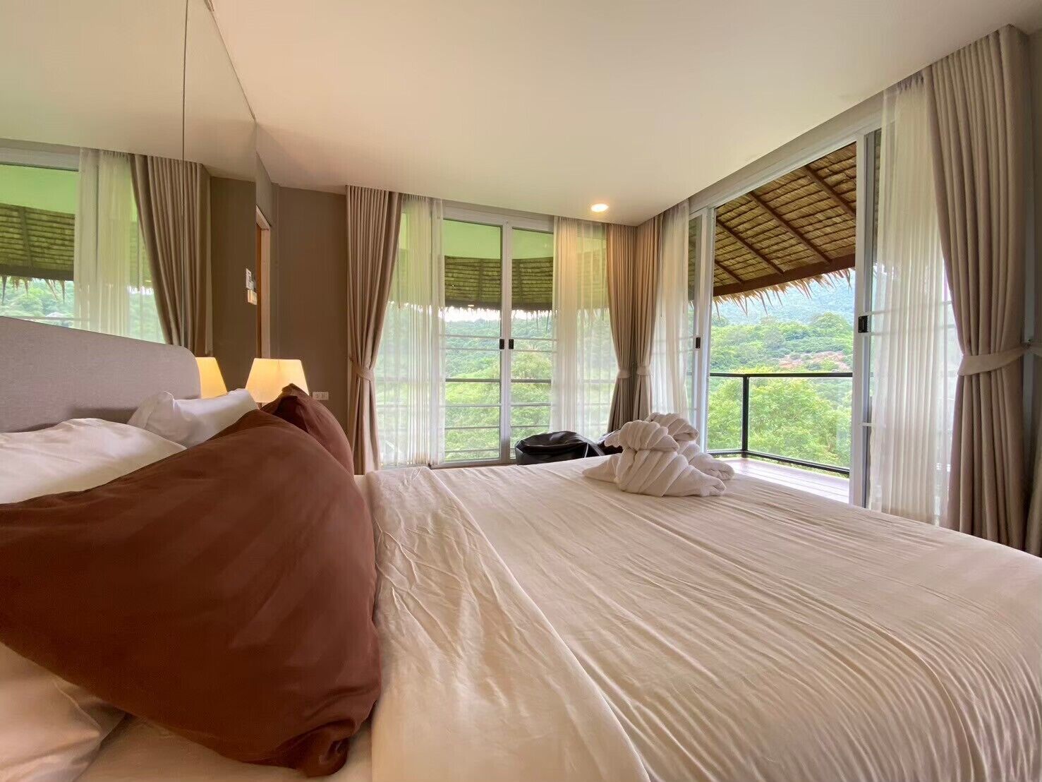 A hotel room with a bed, curtains, a window with a view, and a ceiling fan.