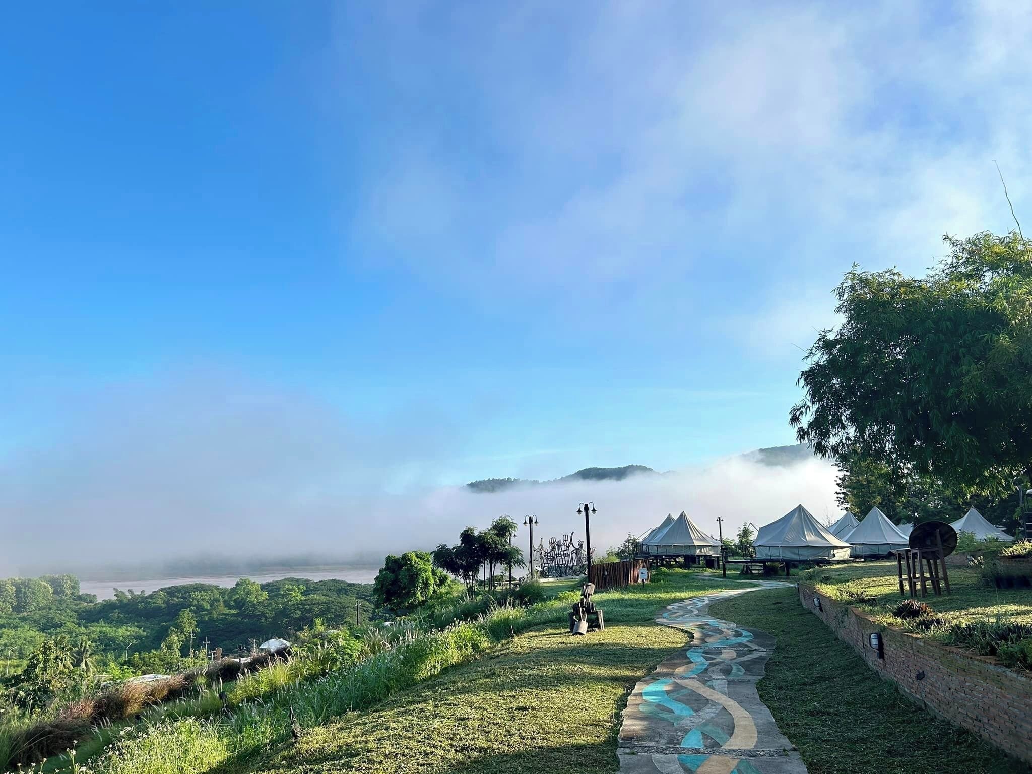 A pathway leading to a series of tents in a lush, green landscape with a clear sky.