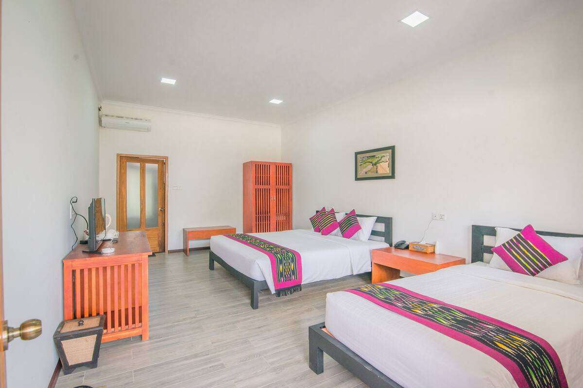 A hotel room with two beds, a desk, a wardrobe, and a ceiling light.