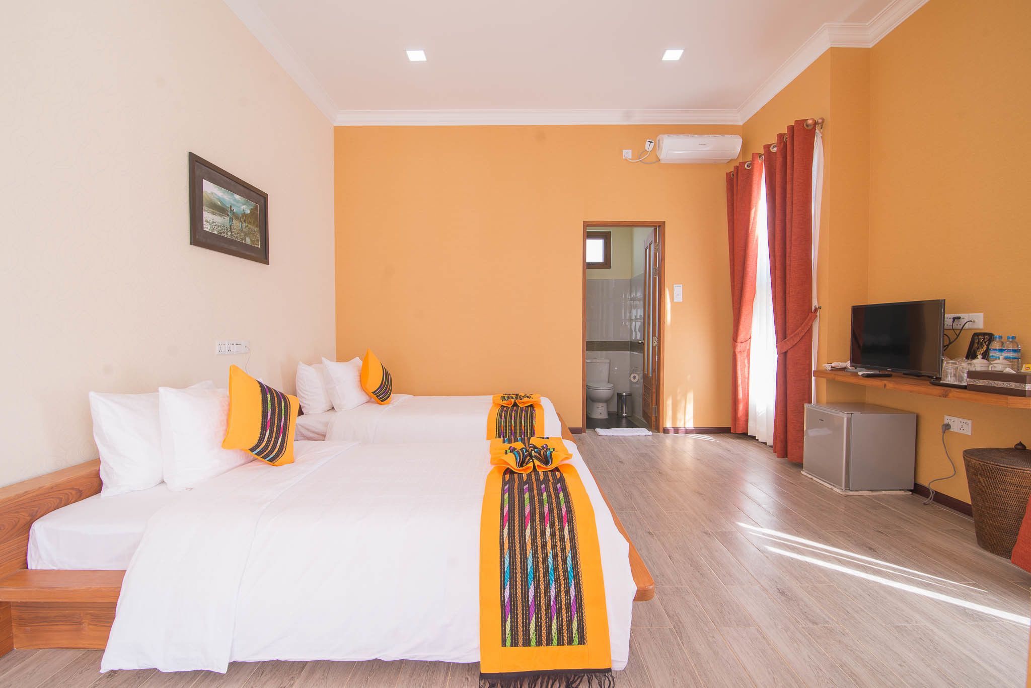 Une chambre d’hôtel avec un grand lit, une télévision, un petit réfrigérateur et une salle de bain visible à travers une porte ouverte.