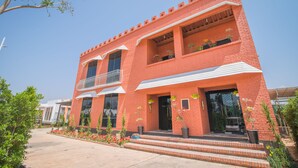 A red brick building with a balcony, steps leading to the entrance, and potted plants.