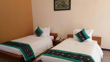 Two single beds with white linens and green accents, a small bedside table with a lamp, and a framed picture on the wall.
