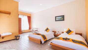 A hotel room with two beds, a wooden bench, a chair, a small table, and a window with curtains.