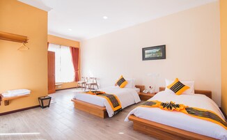 Habitación de hotel con dos camas, un banco de madera, una silla, una mesita y una ventana con cortinas.