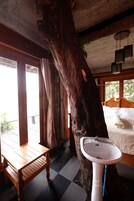 Una habitación rústica con una cama de madera, un lavabo blanco y un gran tronco de árbol.