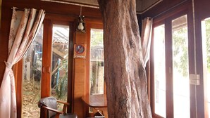Ein rustikales Badezimmer mit einem großen Baumstamm, einem weißen Waschbecken und einem Fenster mit Blick nach draußen.