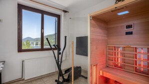 Un sauna avec un banc en bois, une fenêtre donnant sur un pont et des montagnes, ainsi que du matériel d’exercice.
