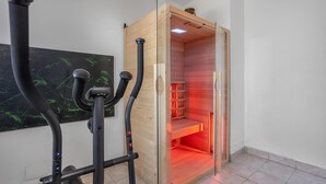 Un sauna avec un intérieur en bois et des portes en verre, un appareil d’exercice fixé au mur et un sol carrelé.