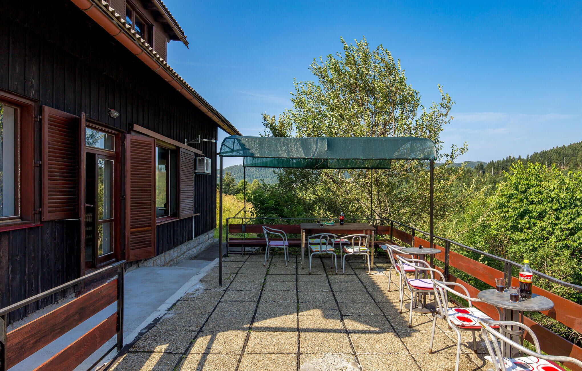A wooden building with a balcony, outdoor seating, and a view of trees and hills.
