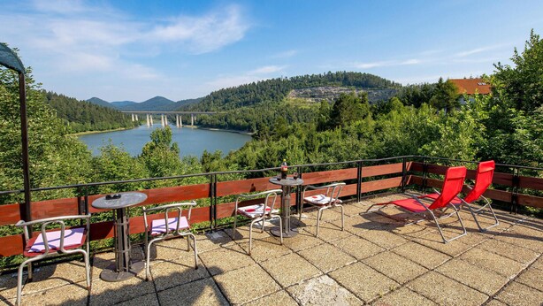 Une terrasse avec des sièges extérieurs, une vue sur un pont enjambant un lac et une végétation luxuriante tout autour.
