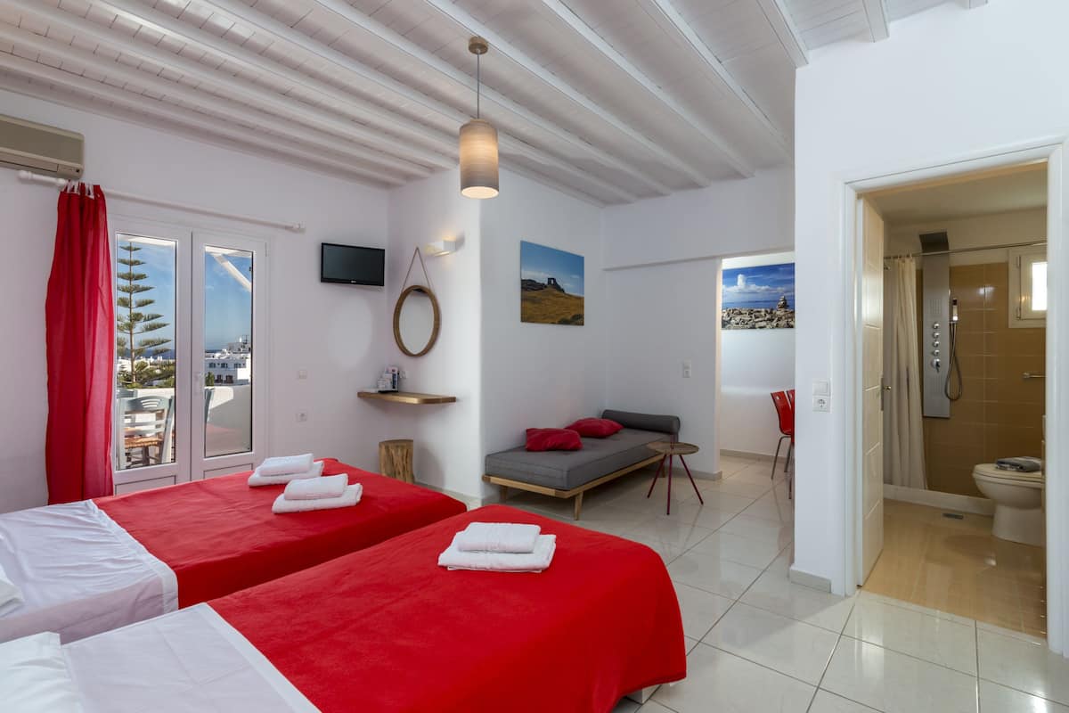 A hotel room with two beds, a sofa, a TV, a shower, and a balcony with a red curtain.