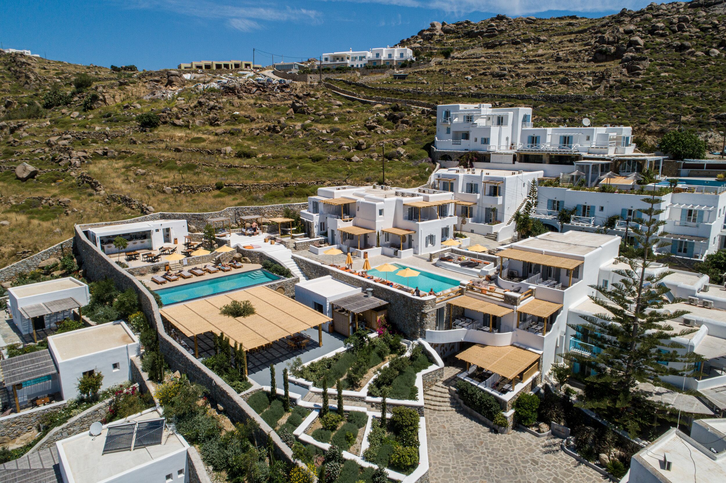 Un moderno resort con piscina, varias edificaciones y un paisaje montañoso de fondo.
