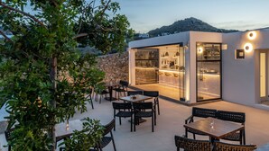 Eine Terrasse im Freien mit Tischen und Stühlen, eine Steinsäule und ein moderner Küchenbereich mit Glastüren.