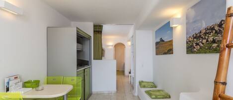 A narrow hallway with a dining area on the left, a kitchen area, and a seating area with cushions on the right.
